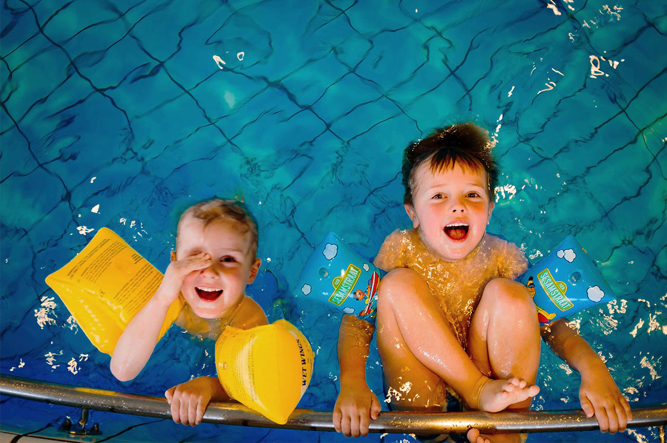 two young boys in a swimming pool laughing with arm bands